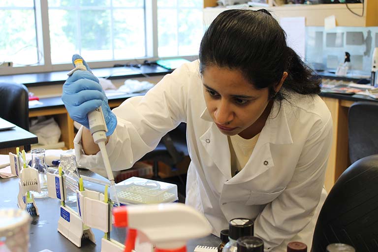 Female student in white lab coat working in lab.