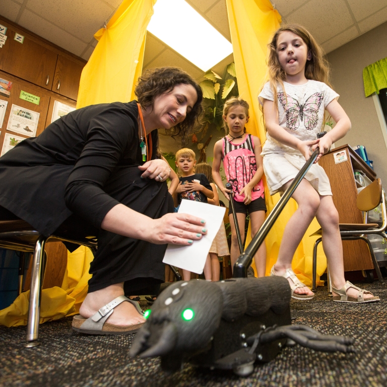 IU researcher Kylie Peppler helps students at Clear Creek Elementary use BioSim wearable technology. A young female student pushes the ant toy.