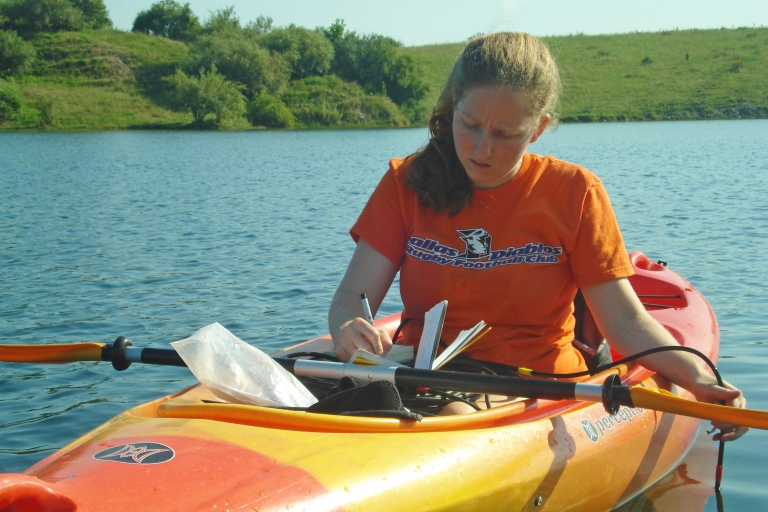 Marta Shocket making research notes while sitting in kayak on lake.