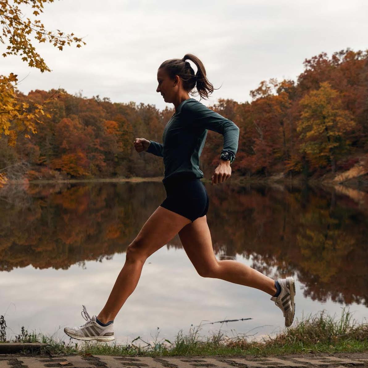 Olivia Ballew runs past a lake as she trains for a marathon. Beautiful fall foliage in the background.