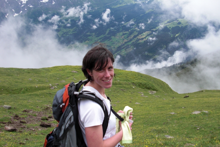 Jen Lau standing on grassy hilltop with valley and another hill shrouded by clouds in the background.