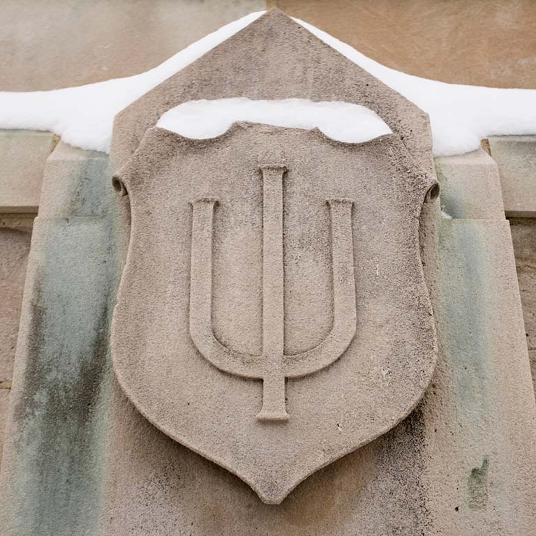 IU trident carved in limestone extends from an outside wall. Snow rests on the top of the engraving.