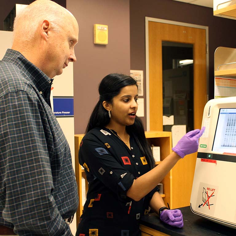 John Patton watches as Asha Philip explains the images on the computer screen in the lab.