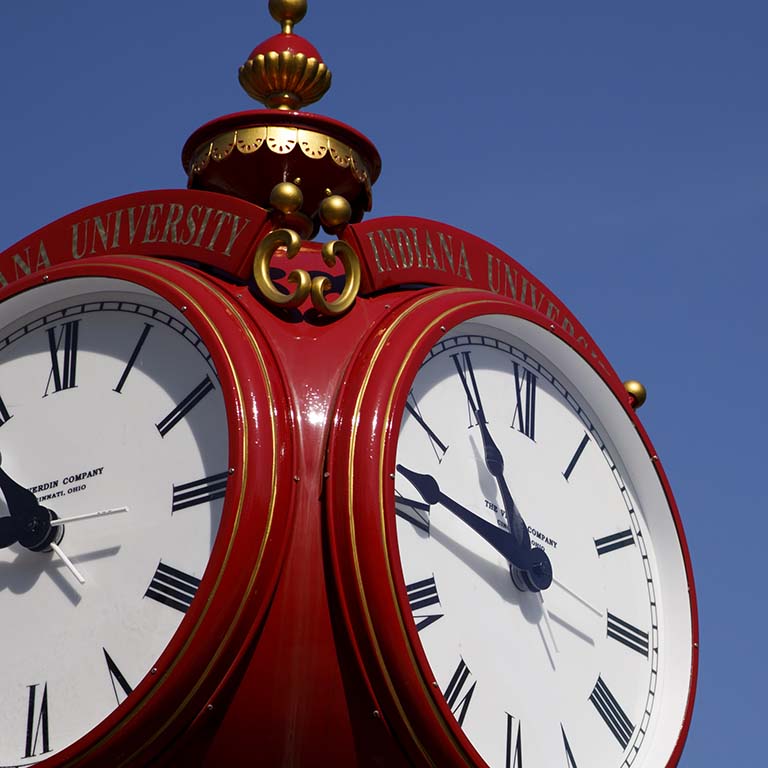 IU Bloomington's iconic red clock against a clear blue sky.